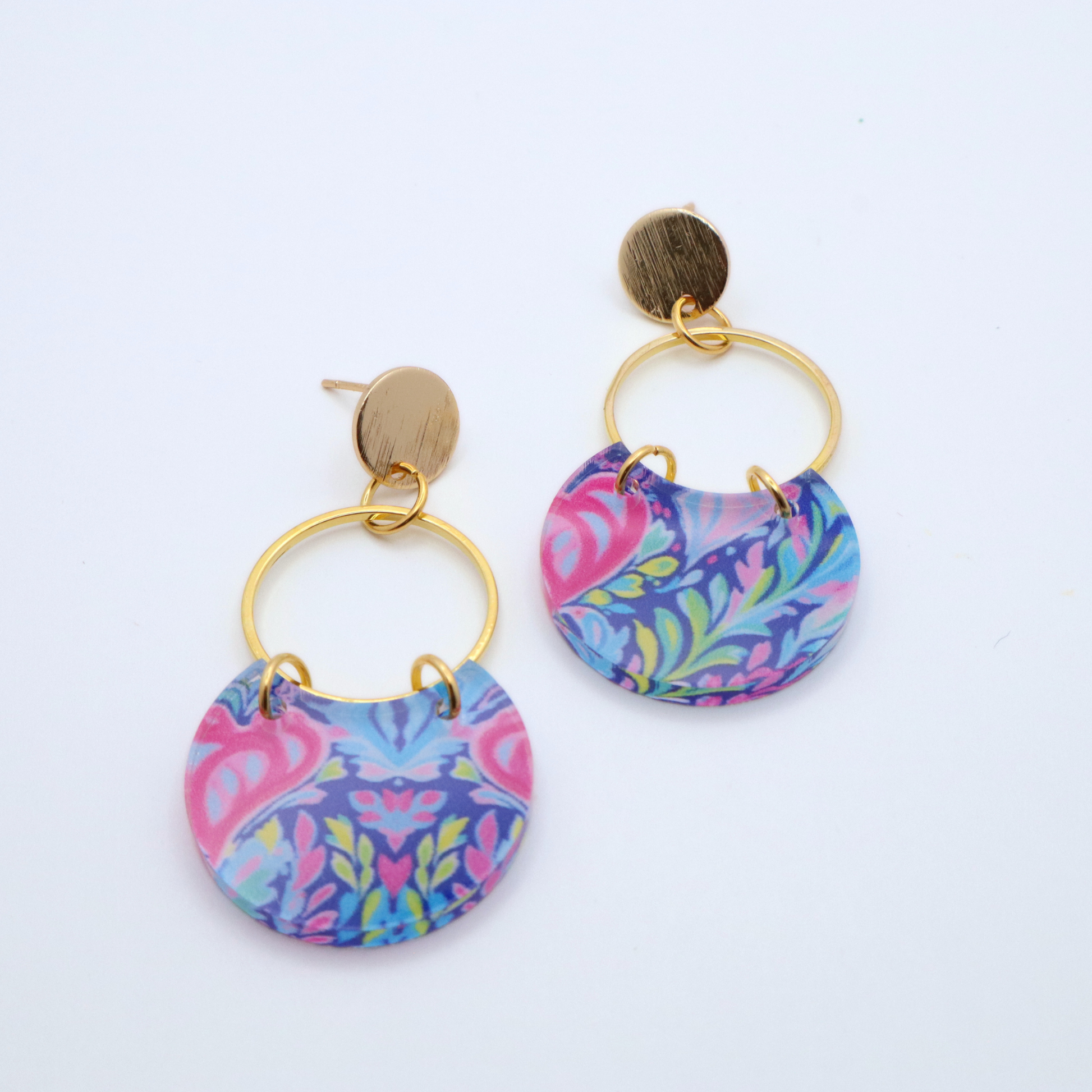 Handmade acrylic earrings with multicolor floral and scroll pattern attached to gold hoop and 18k gold plated stud posts shown flat lay