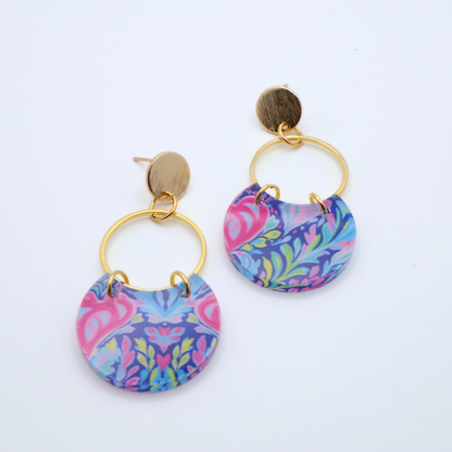 Handmade acrylic earrings with multicolor floral and scroll pattern attached to gold hoop and 18k gold plated stud posts shown flat lay