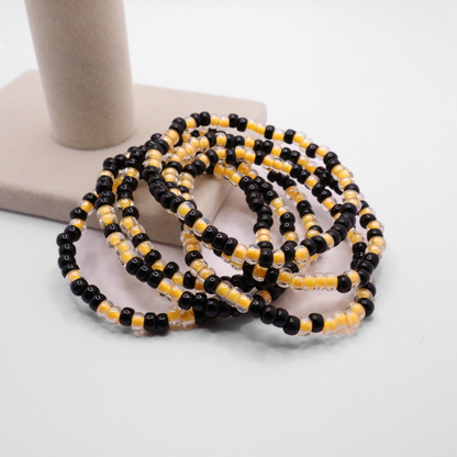 Set of six black and gold seed bead stretch bracelets featuring random black and gold seed beads on a white background