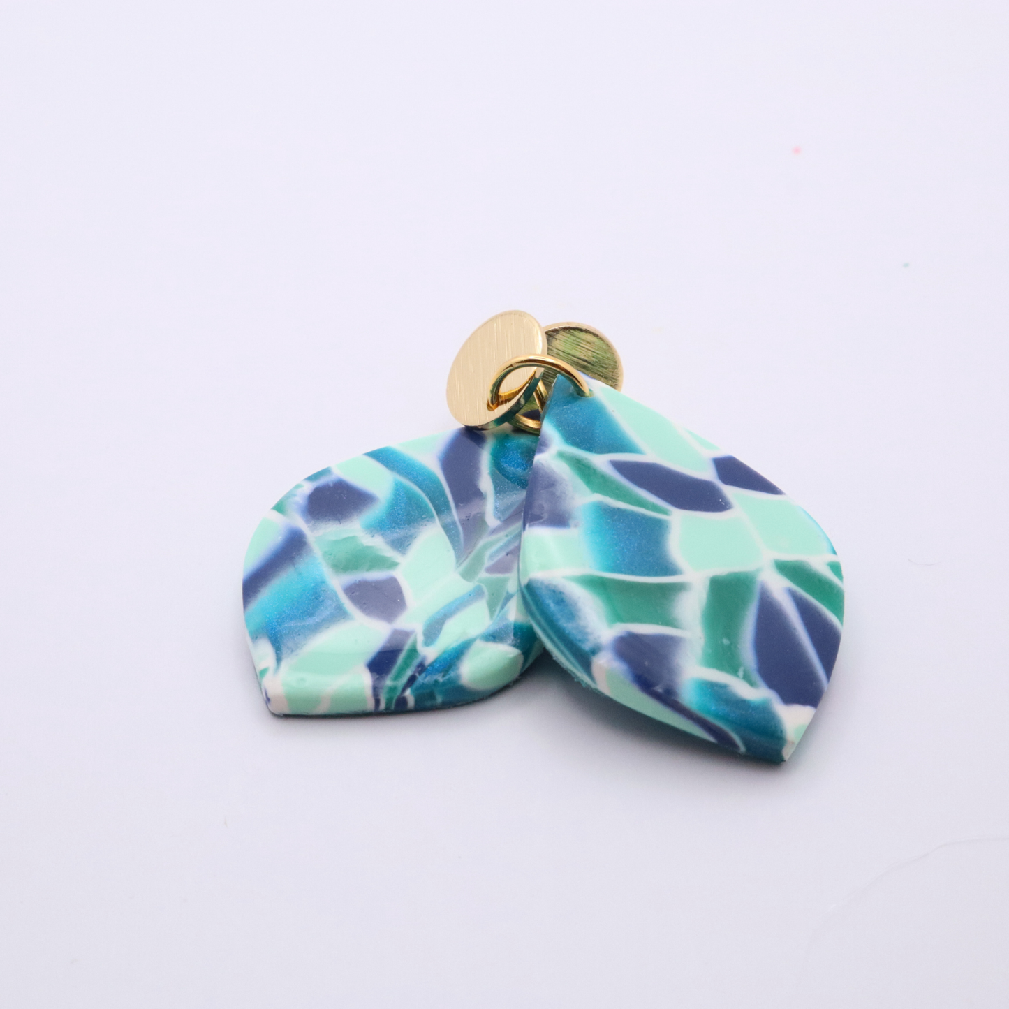Stacked view of teal and navy marbled teardrop earrings with 18k gold plated studs highlighting layered design