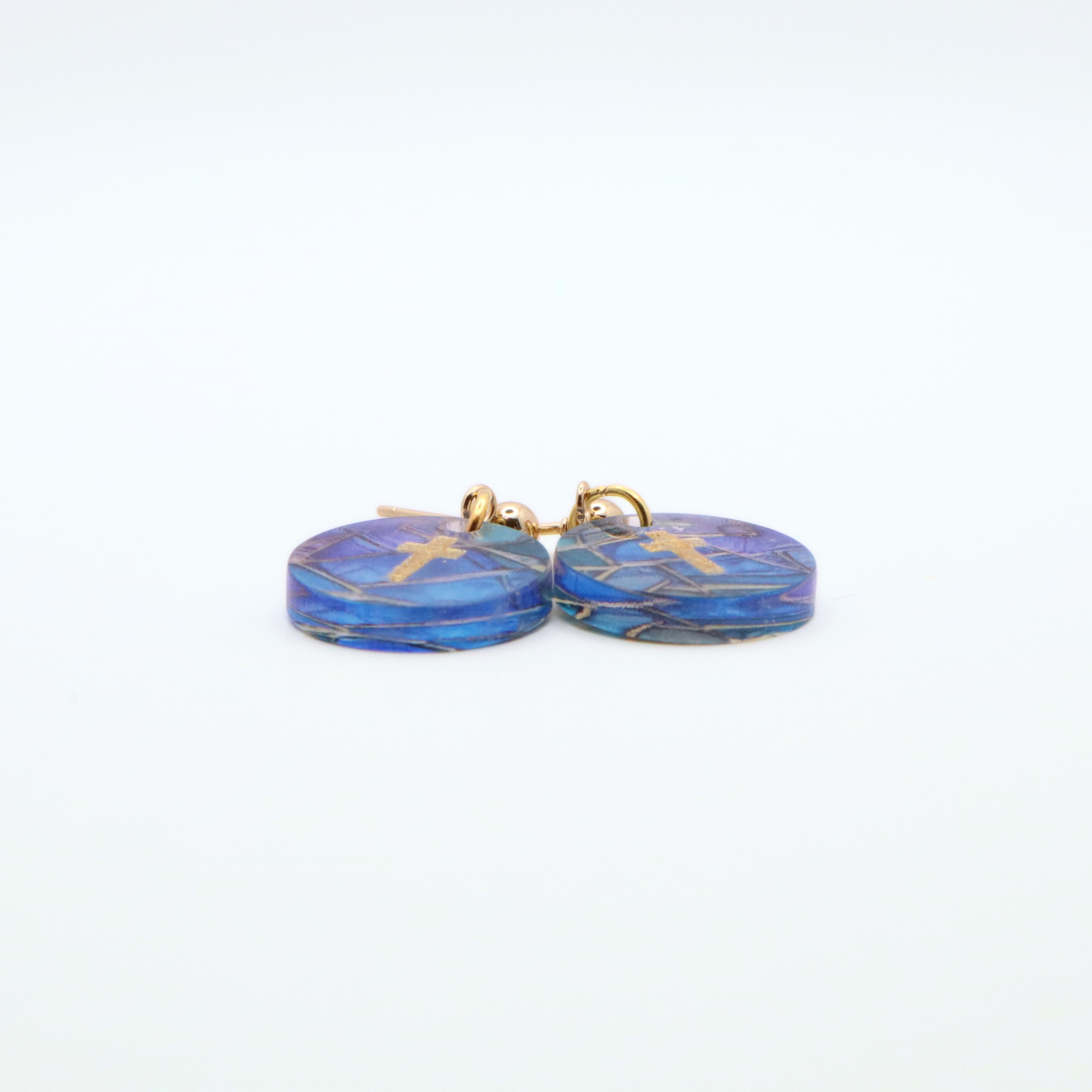Side view of acrylic cross earrings showing thickness and glossy finish with blue stained glass pattern and gold cross detail on stainless steel posts