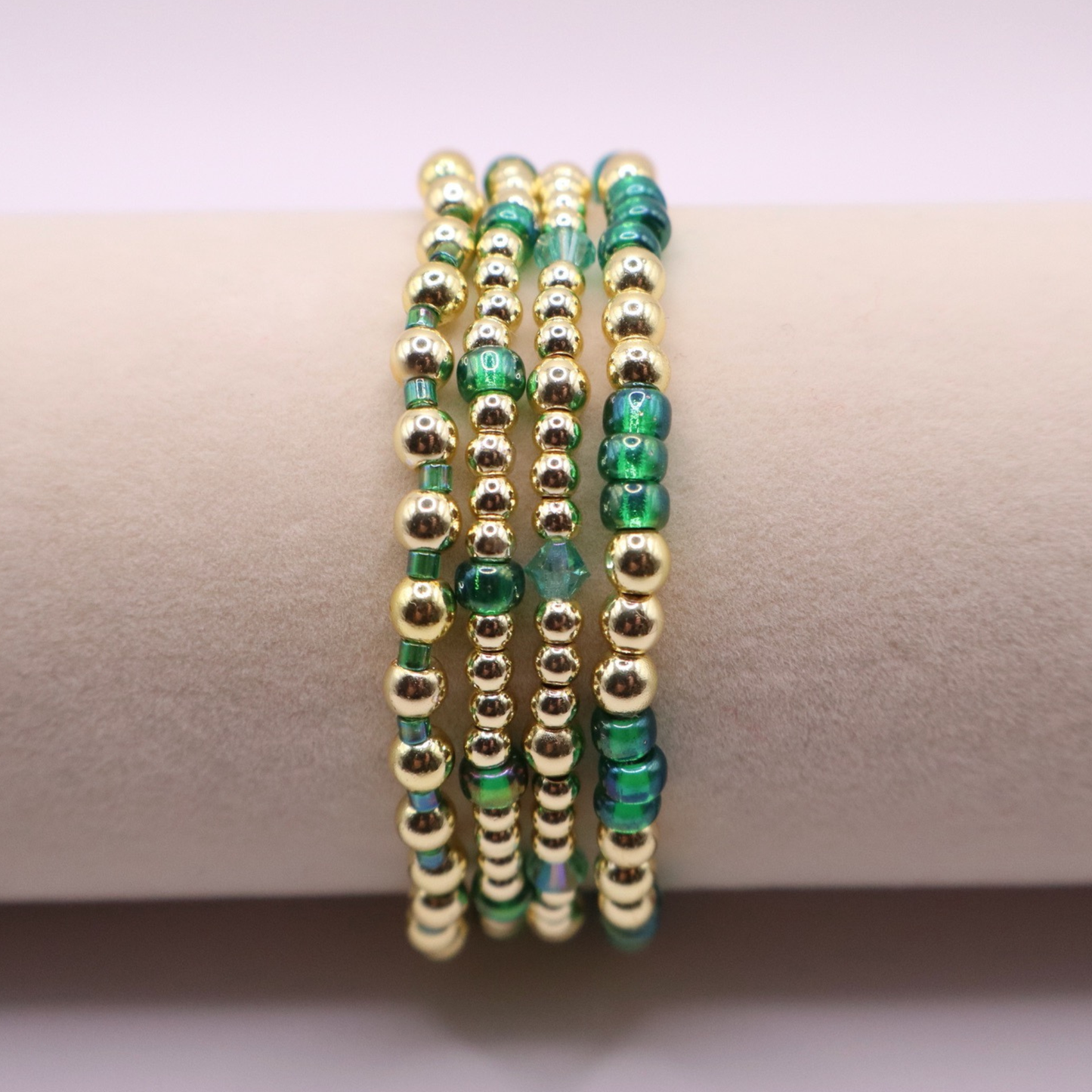 Handmade bracelet stack with green Preciosa seed beads, iridescent crystal accents, and polished gold-tone hematite beads on a clean white background.