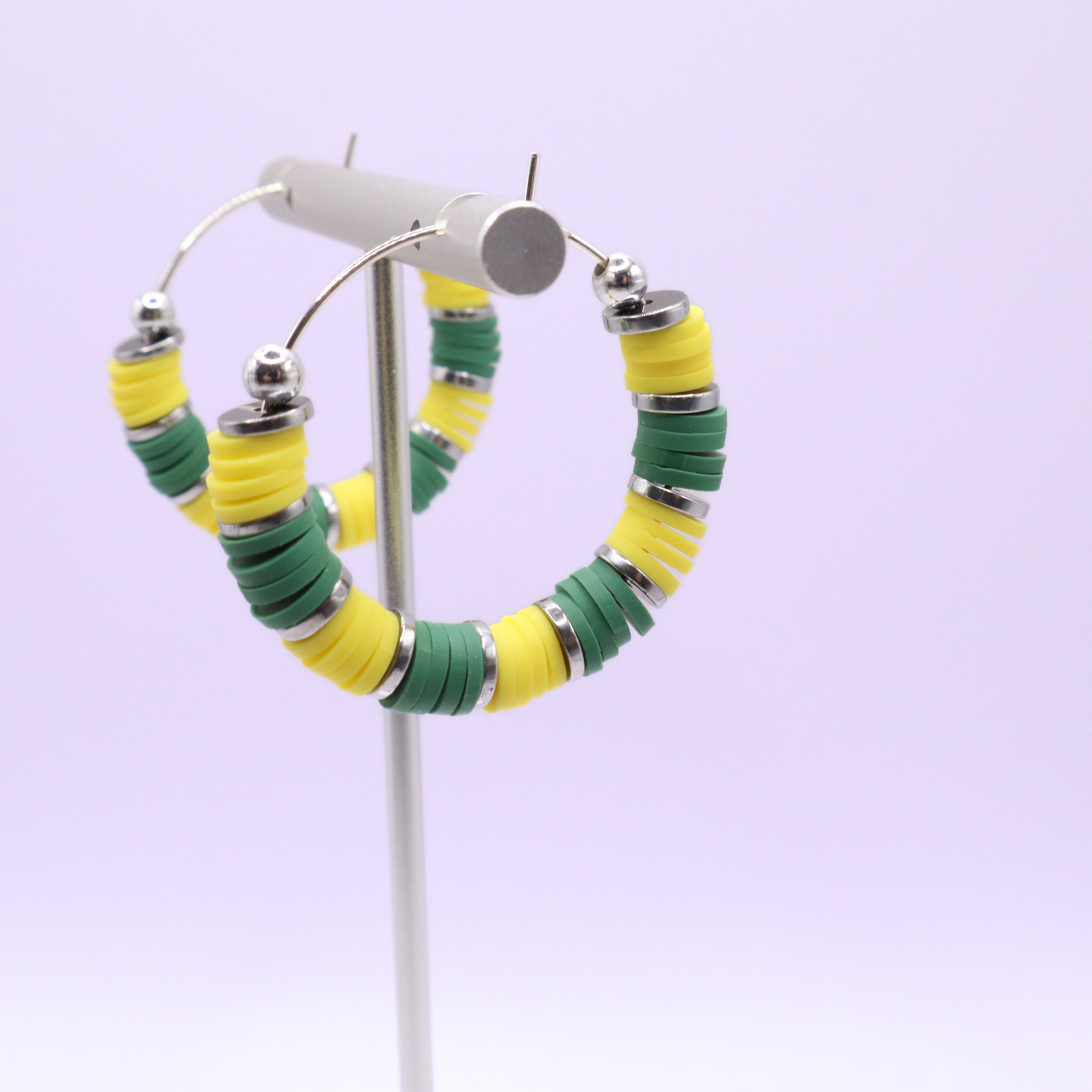 Green and yellow heishi bead hoop earrings with silver accents displayed on a branded card against a white background