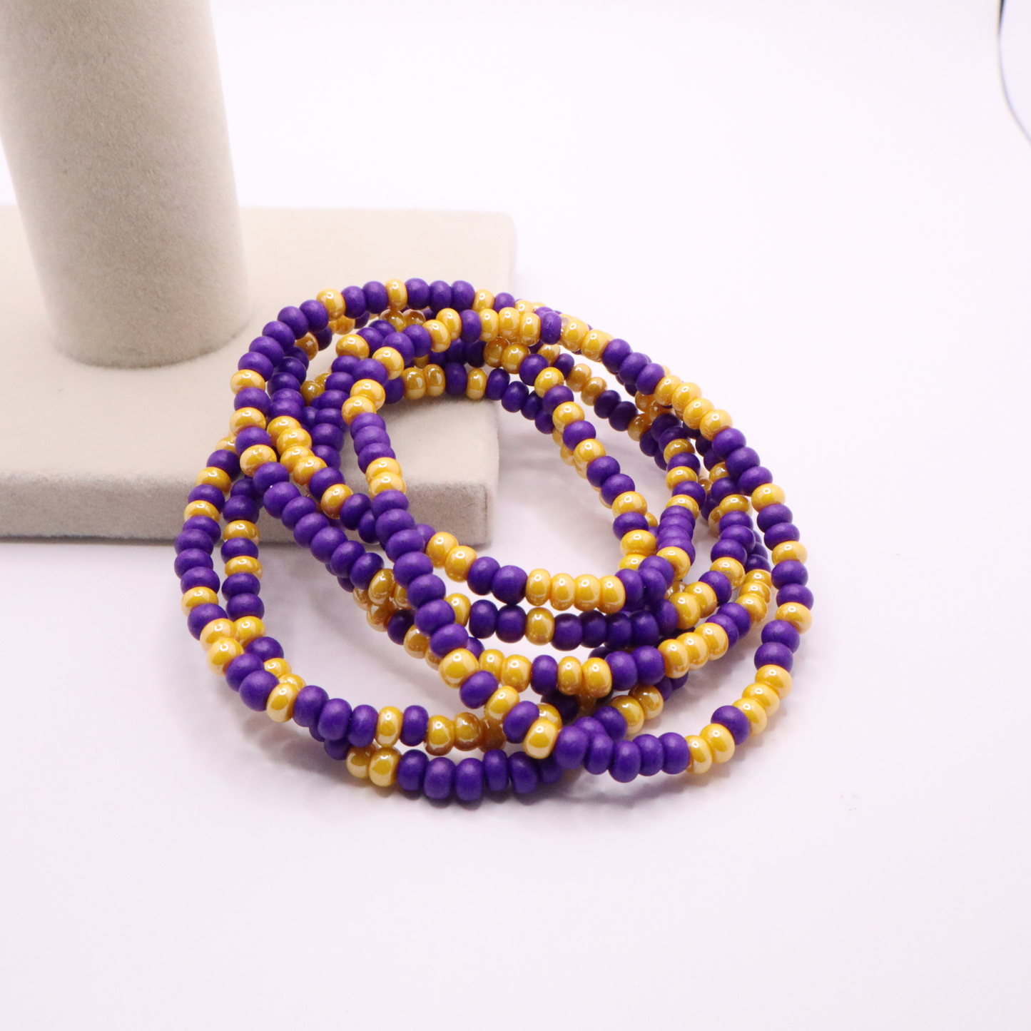 Set of six purple and gold seed bead stretch bracelets featuring random purple and gold seed beads on a white background