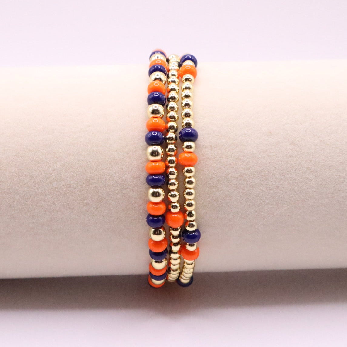 three navy blue, orange, and gold beaded bracelets on a bracelet display