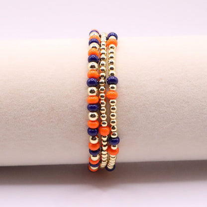 three navy blue, orange, and gold beaded bracelets on a bracelet display
