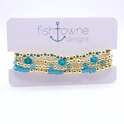 Layered periwinkle and gold bracelet stack displayed on a jewelry stand.