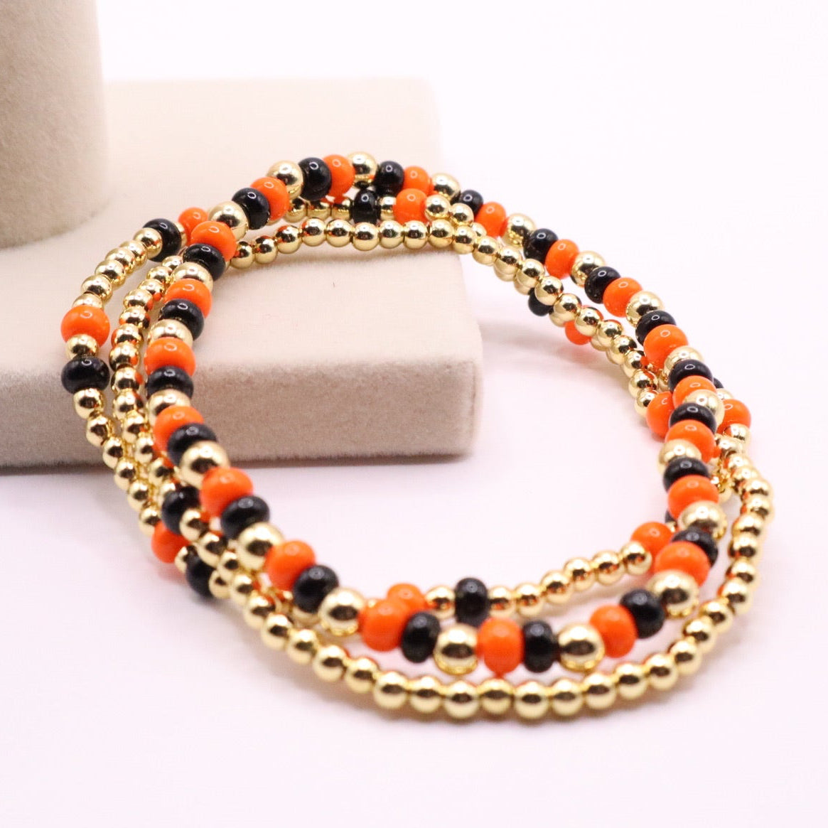 Stack of beaded bracelets with orange and black beads on a white background