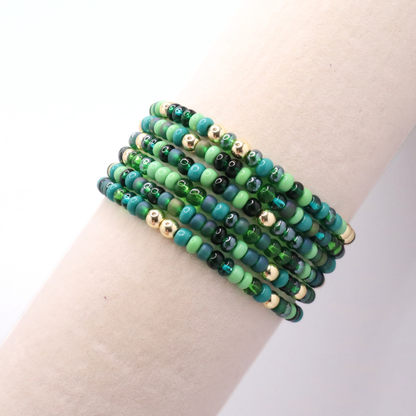 Set of six green and gold beaded bracelets on a wrist against a white background