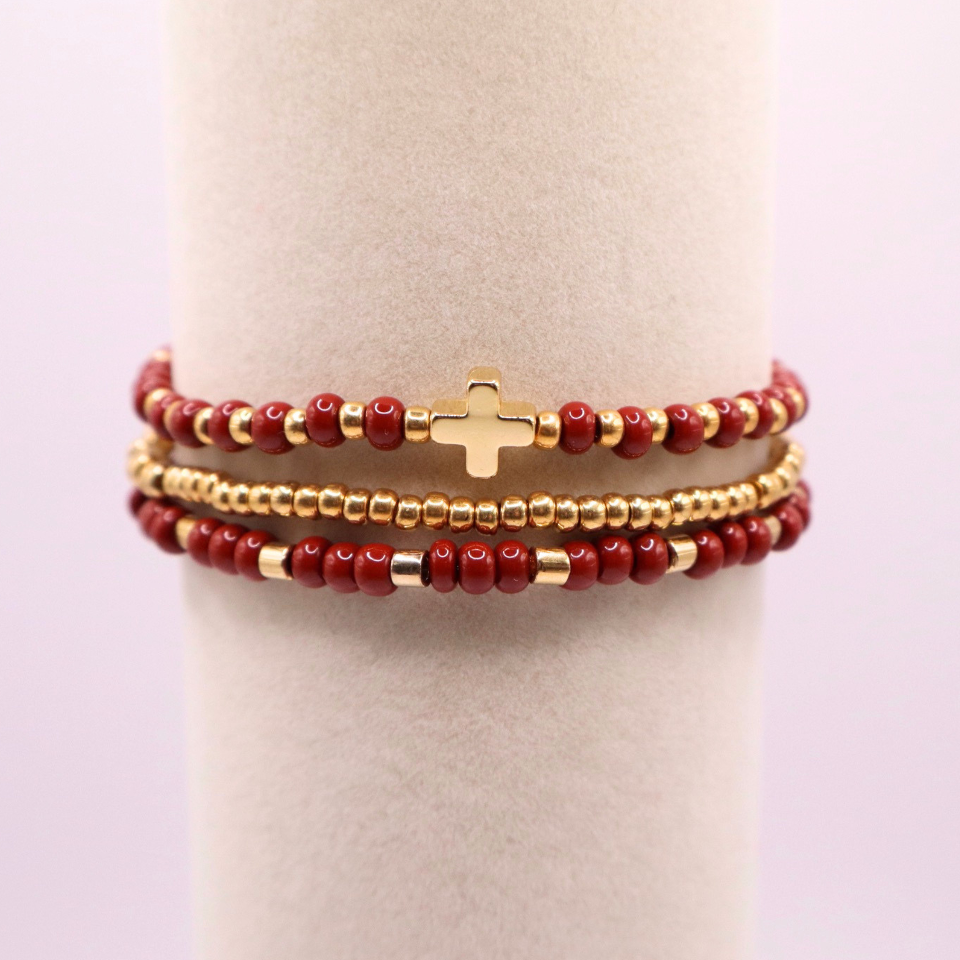 Stack of rust beaded bracelets with gold accents on a white stand.
