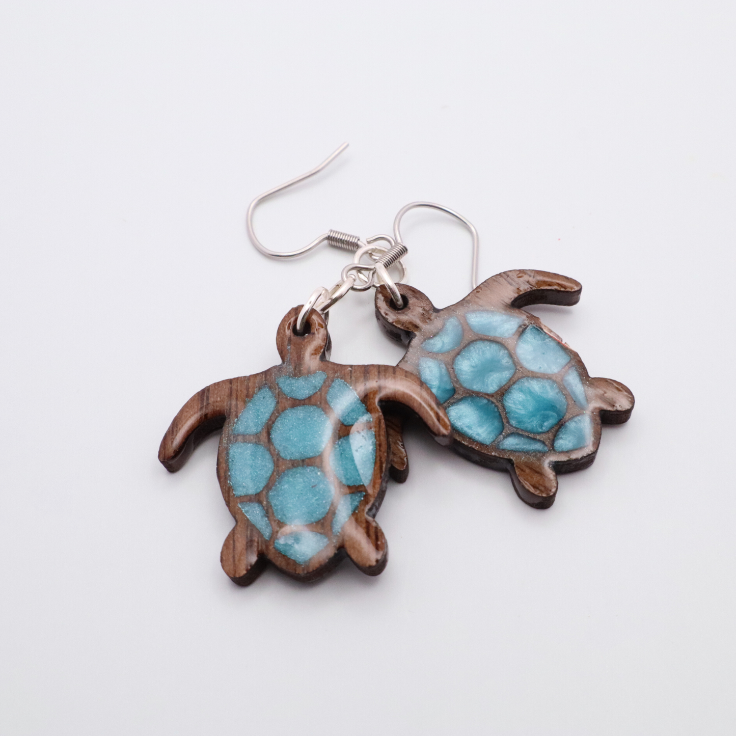 Turtle-shaped black walnut earrings with sea glass blue resin on a white background