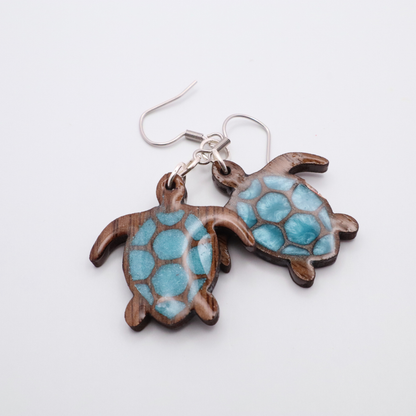 Turtle-shaped black walnut earrings with sea glass blue resin on a white background