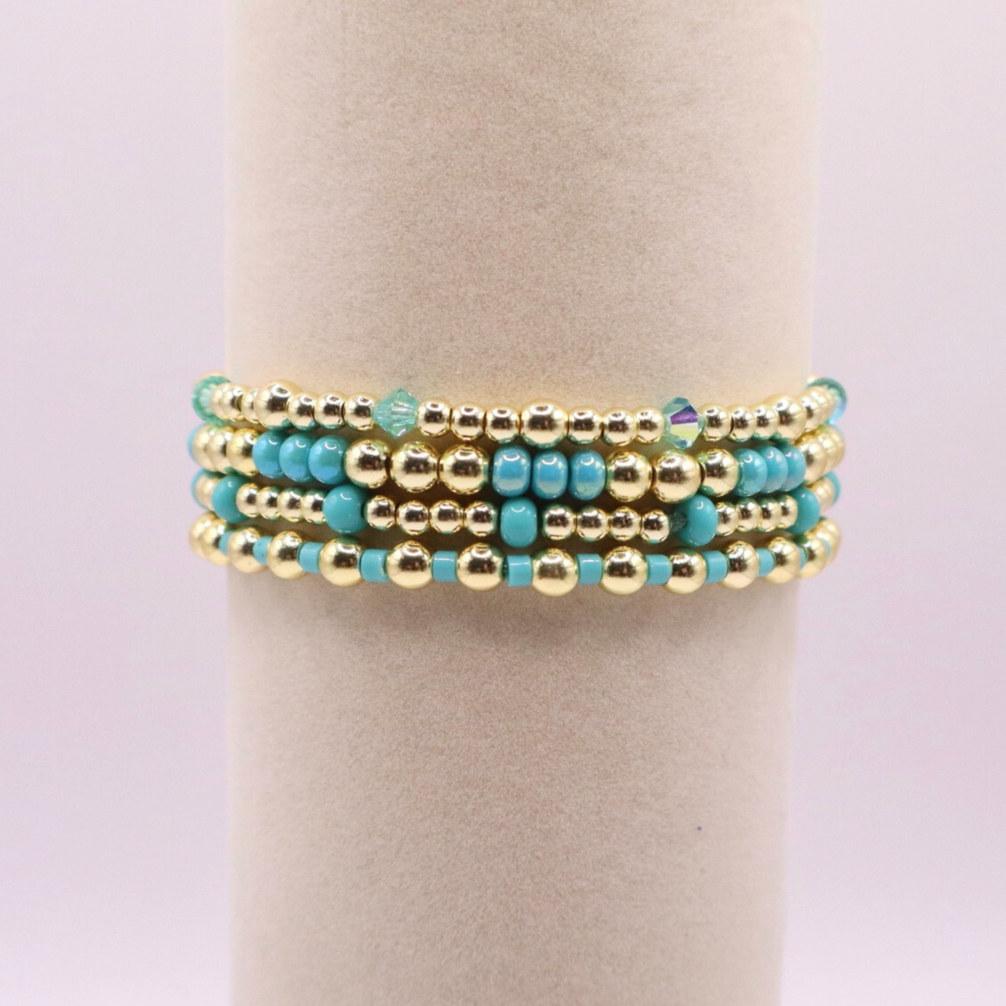 Layered bracelet stack with turquoise Preciosa seed beads, shimmering crystal accents, and gold-tone hematite beads on a clean white background.