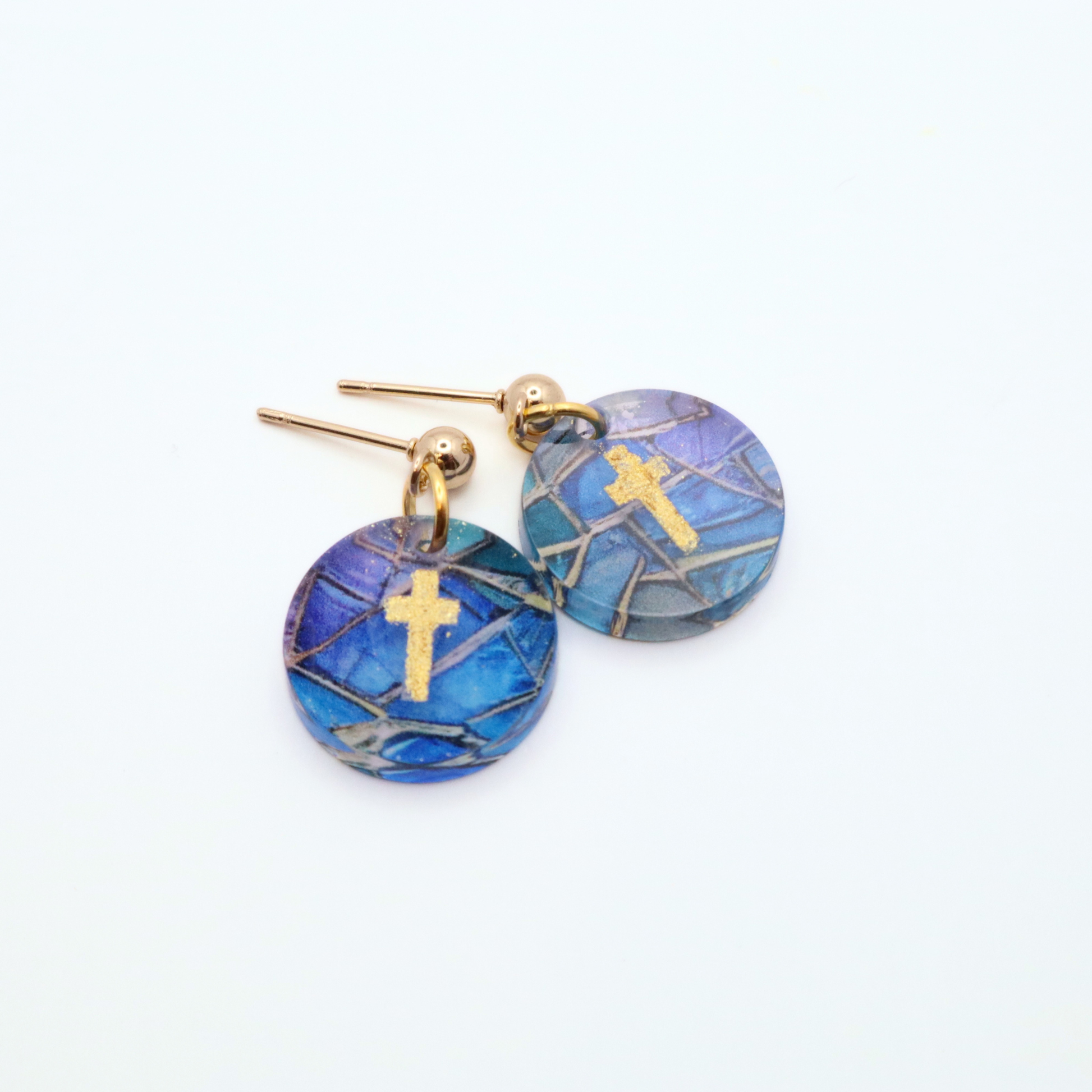 Handmade acrylic cross earrings with blue stained glass pattern and gold cross detail displayed on stainless steel stud posts