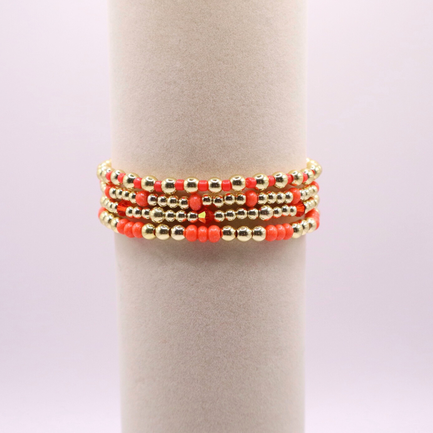 Stack of handmade stretch bracelets featuring vibrant coral Preciosa seed beads, faceted crystal accents, and polished gold-tone hematite beads on a clean white background.