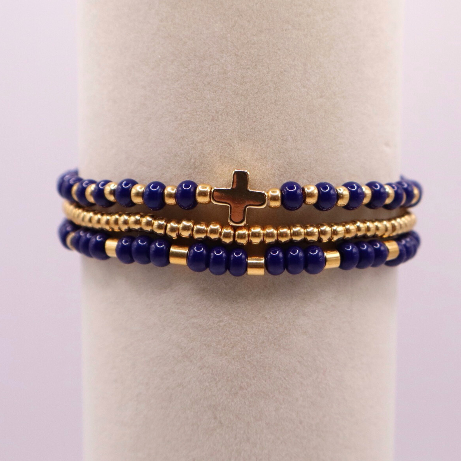 Stack of three navy blue and gold plated beaded bracelets on a white stand