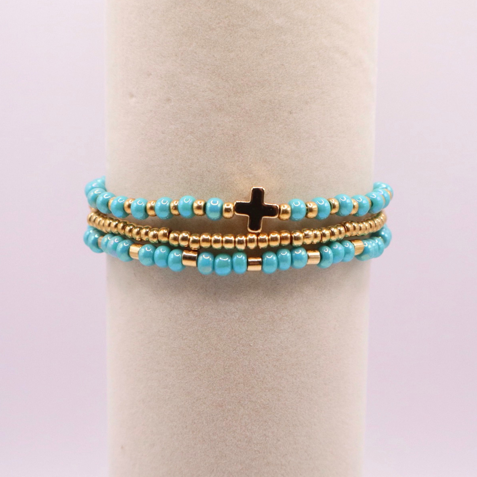Turquoise beaded bracelet stack with gold accents and a cross charm on a white stand.