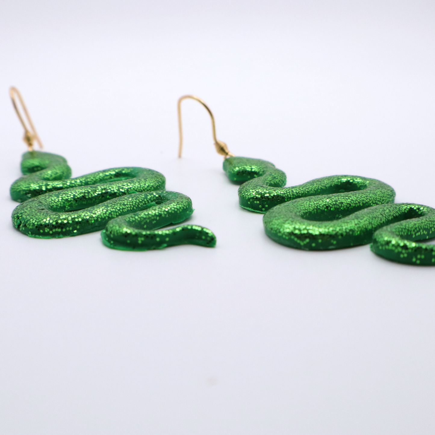 Green glittery snake-shaped earrings on a white background