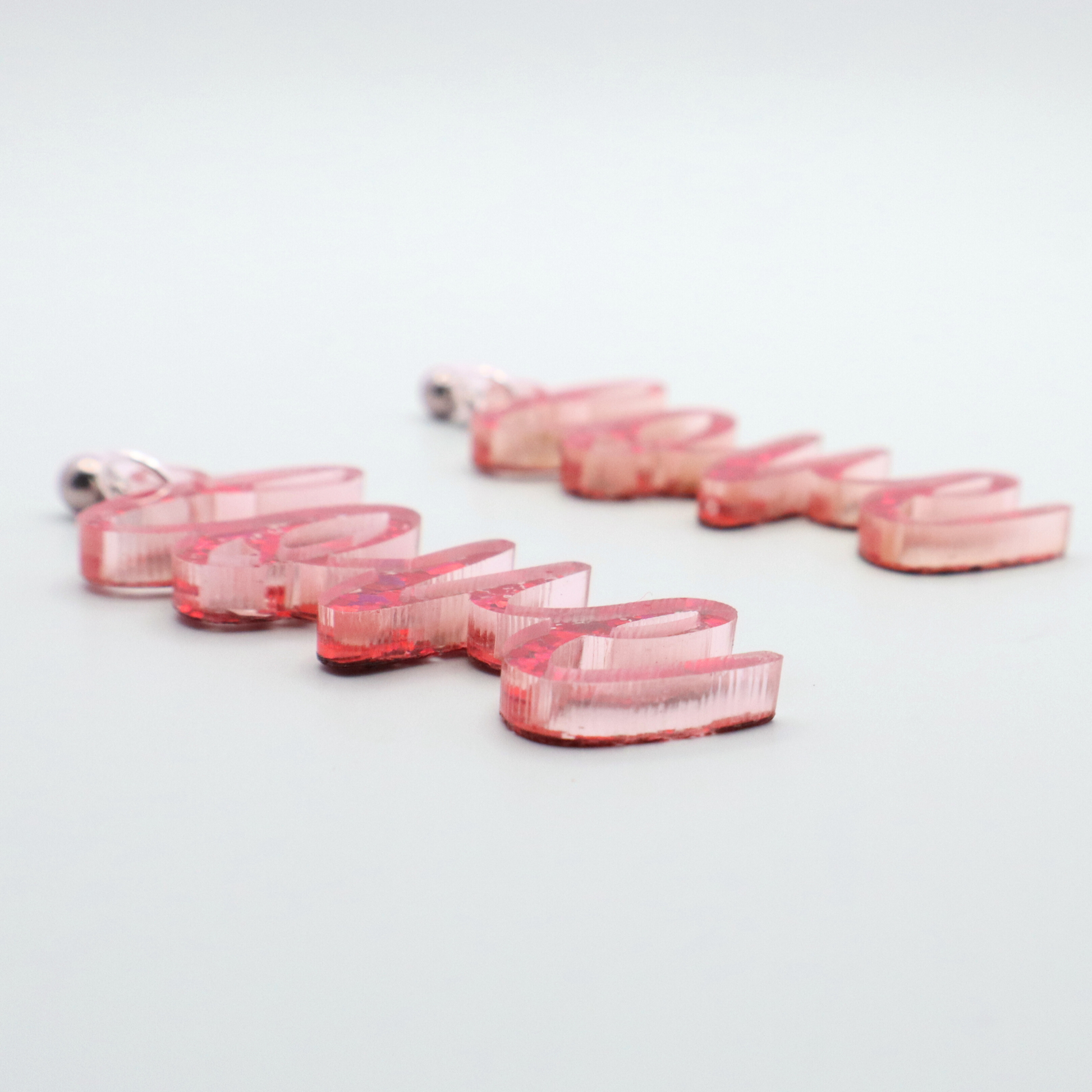 Pink glitter 'love' earrings on a white gray background