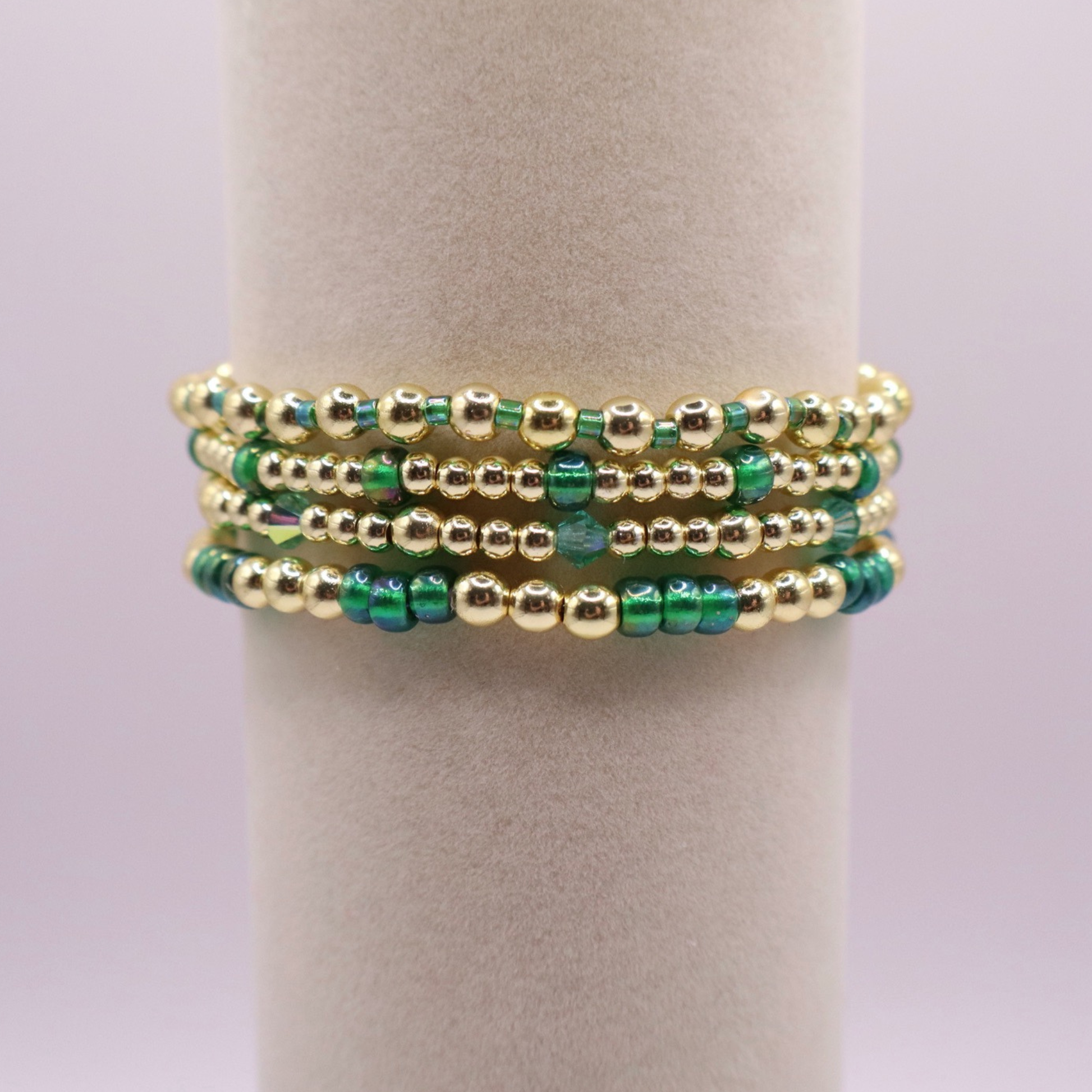 Handmade bracelet stack with green Preciosa seed beads, iridescent crystal accents, and polished gold-tone hematite beads on a clean white background.