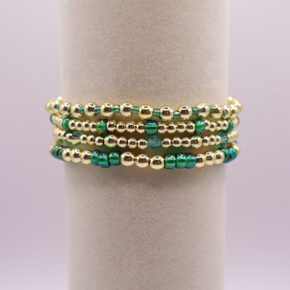 Handmade bracelet stack with green Preciosa seed beads, iridescent crystal accents, and polished gold-tone hematite beads on a clean white background.