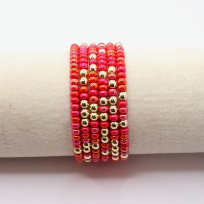 Stack of six pink and gold beaded bracelets on a beige surface
