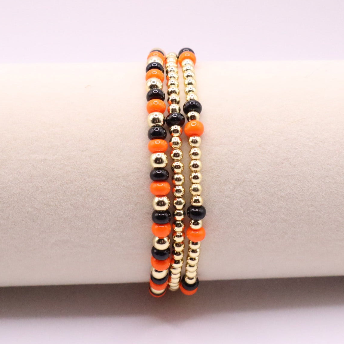 Three orange, black and gold bracelets on a bracelet display