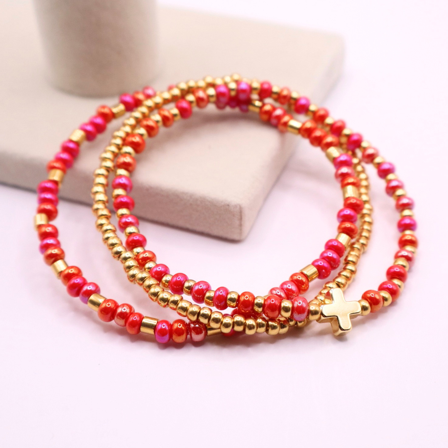Set of pink and gold beaded bracelets with a gold cross charm on a light pink background