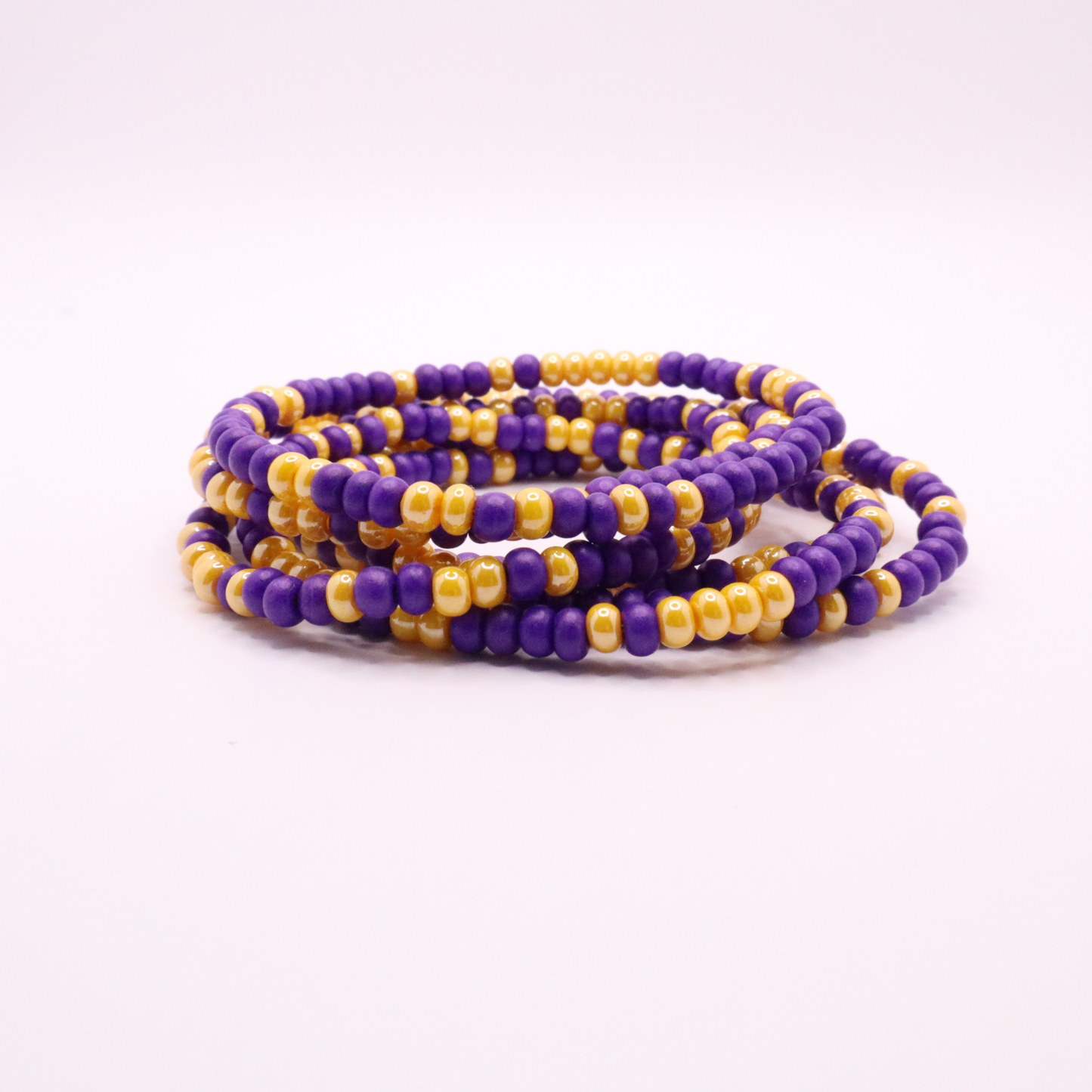 Set of six purple and gold seed bead stretch bracelets featuring random purple and gold seed beads on a white background