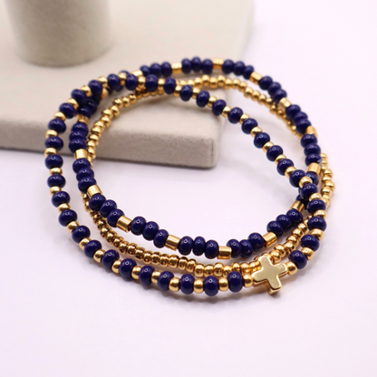 Three gold plated beaded bracelets with gold and navy blue beads on a white surface