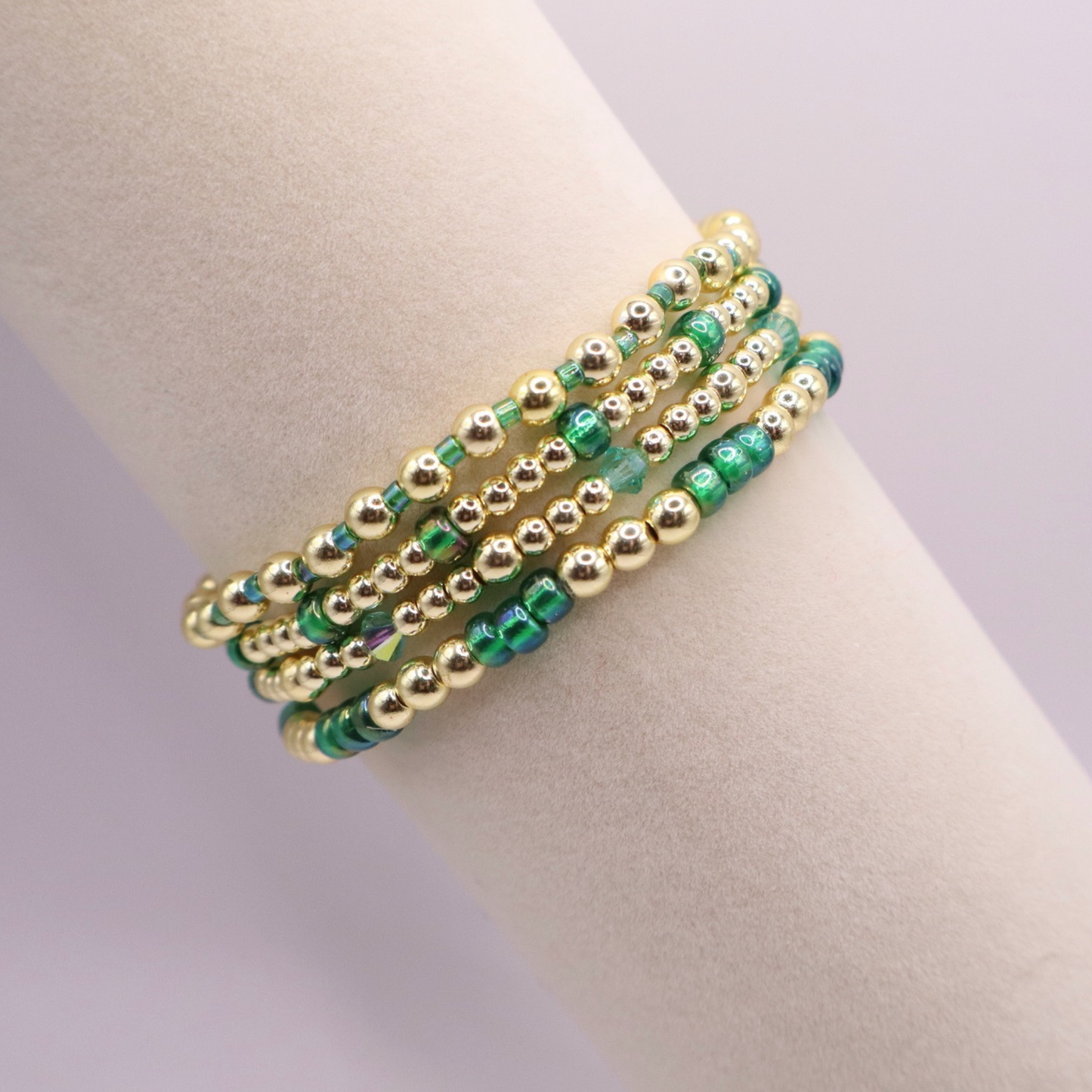 Handmade bracelet stack with green Preciosa seed beads, iridescent crystal accents, and polished gold-tone hematite beads on a clean white background.