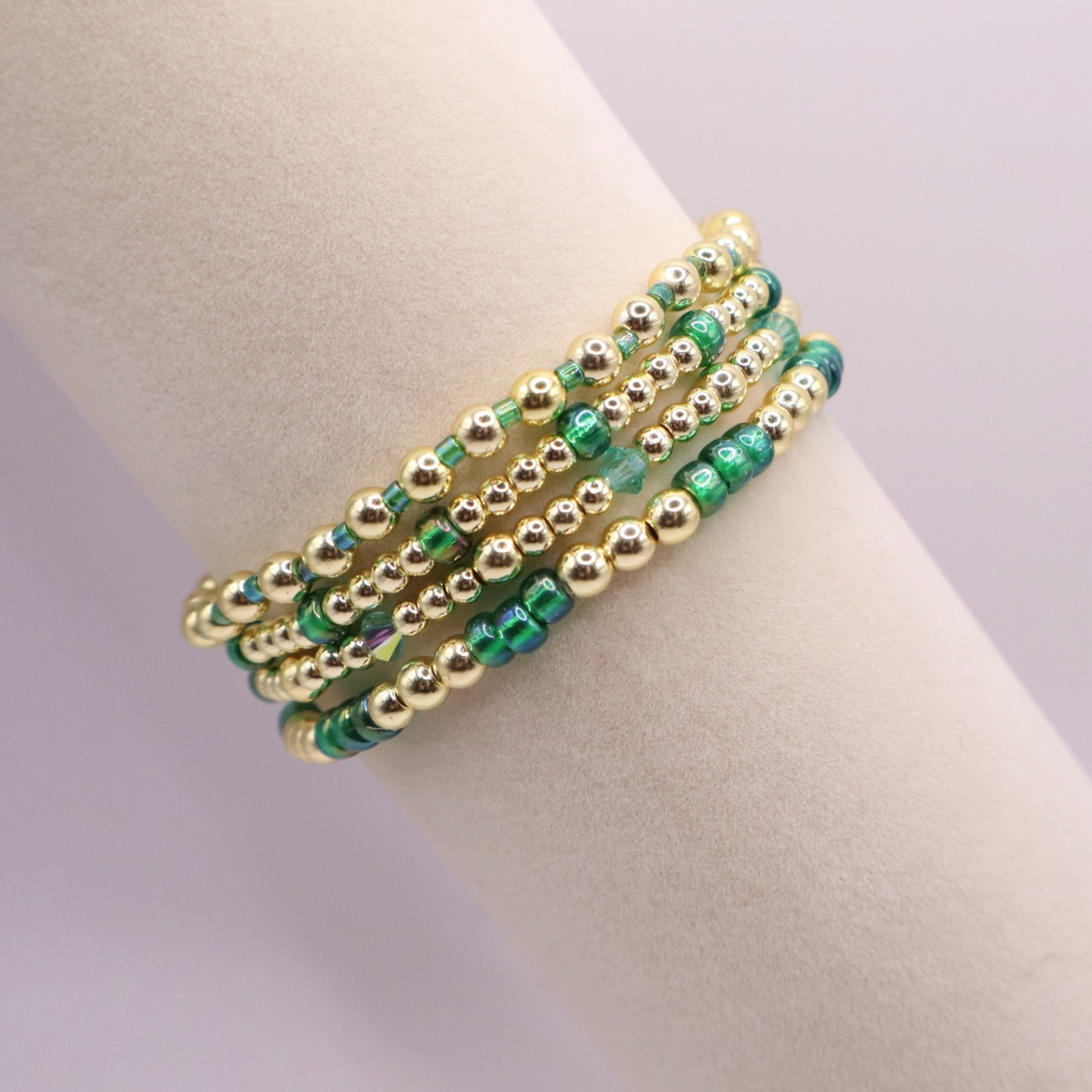 Handmade bracelet stack with green Preciosa seed beads, iridescent crystal accents, and polished gold-tone hematite beads on a clean white background.