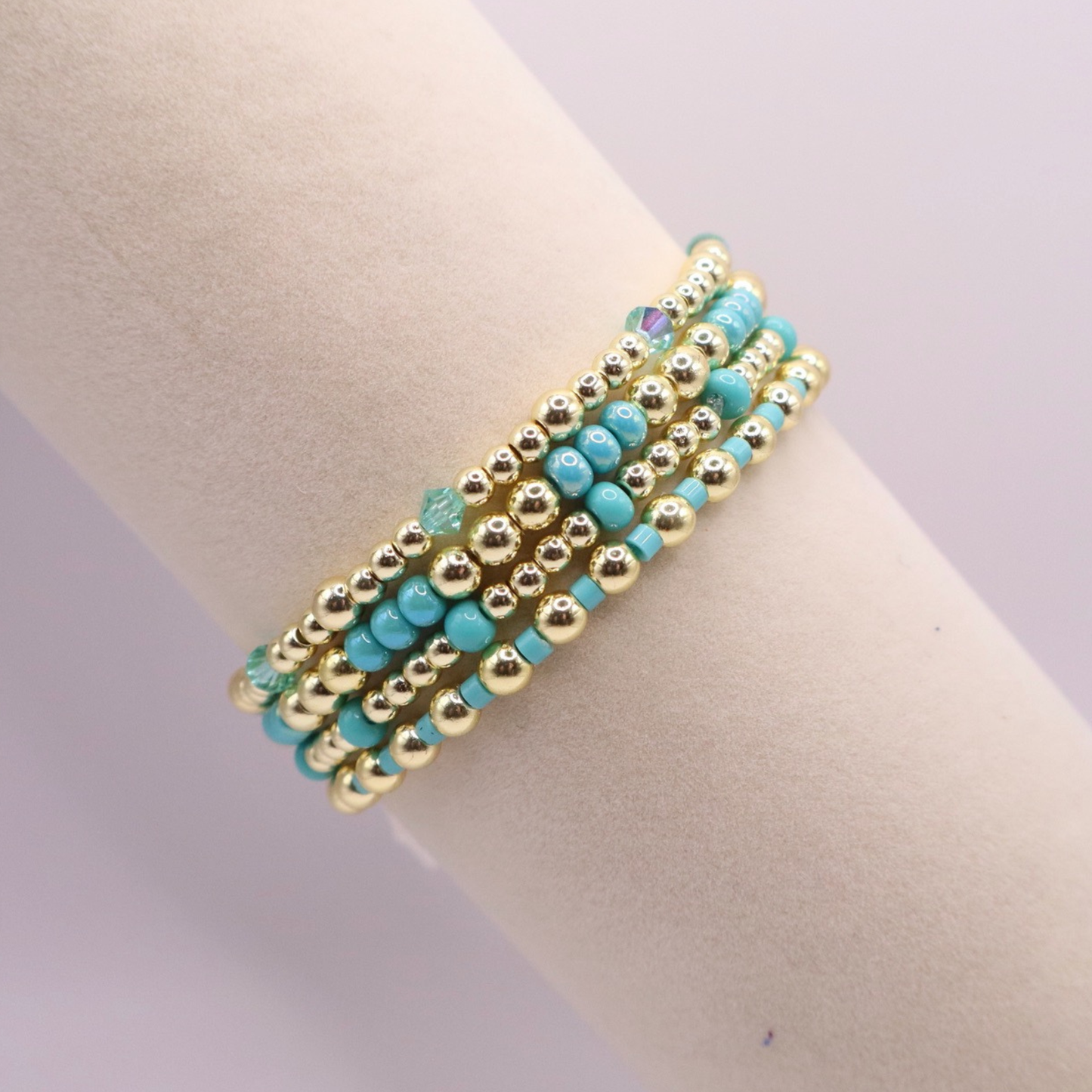 Layered bracelet stack with turquoise Preciosa seed beads, shimmering crystal accents, and gold-tone hematite beads on a clean white background.