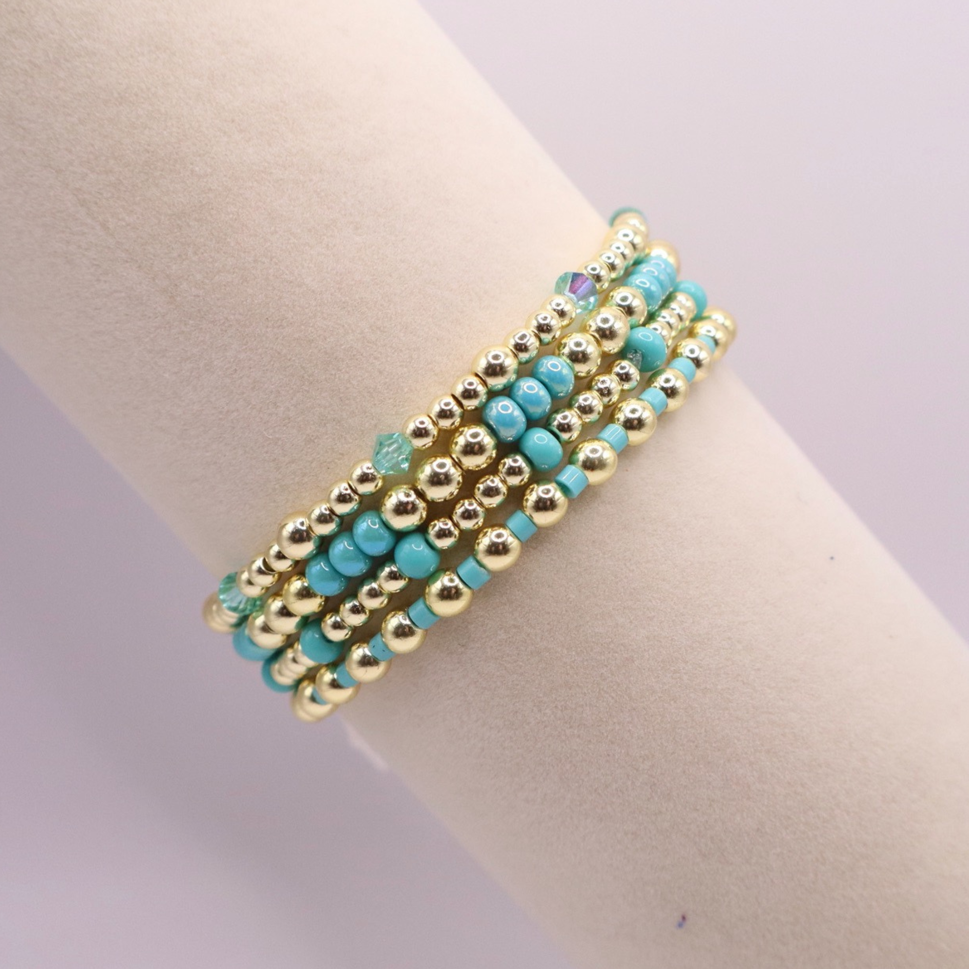Layered bracelet stack with turquoise Preciosa seed beads, shimmering crystal accents, and gold-tone hematite beads on a clean white background.