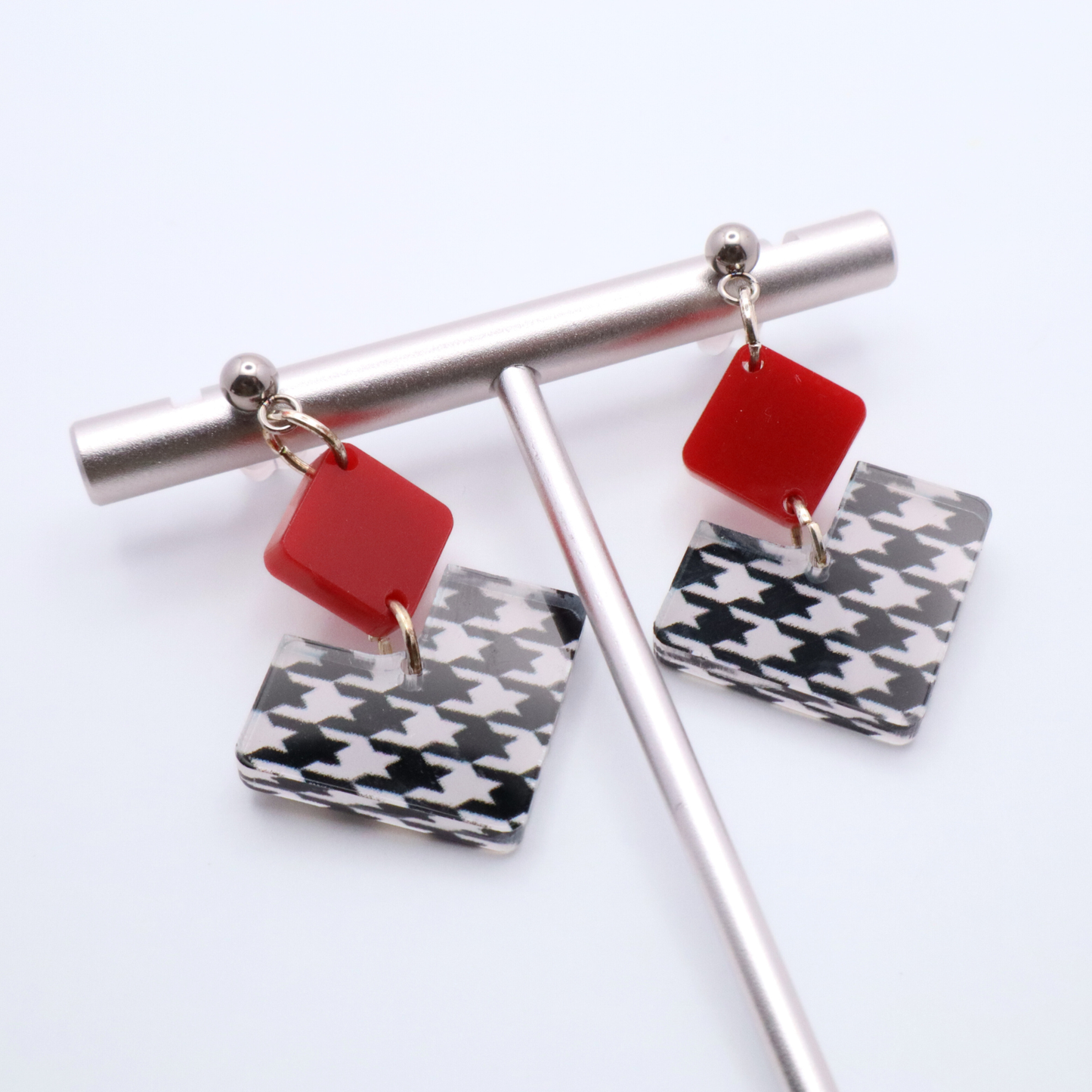Earrings with red and houndstooth patterned charms on a white background