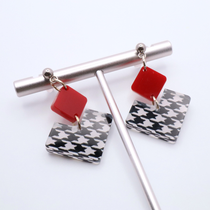 Earrings with red and houndstooth patterned charms on a white background