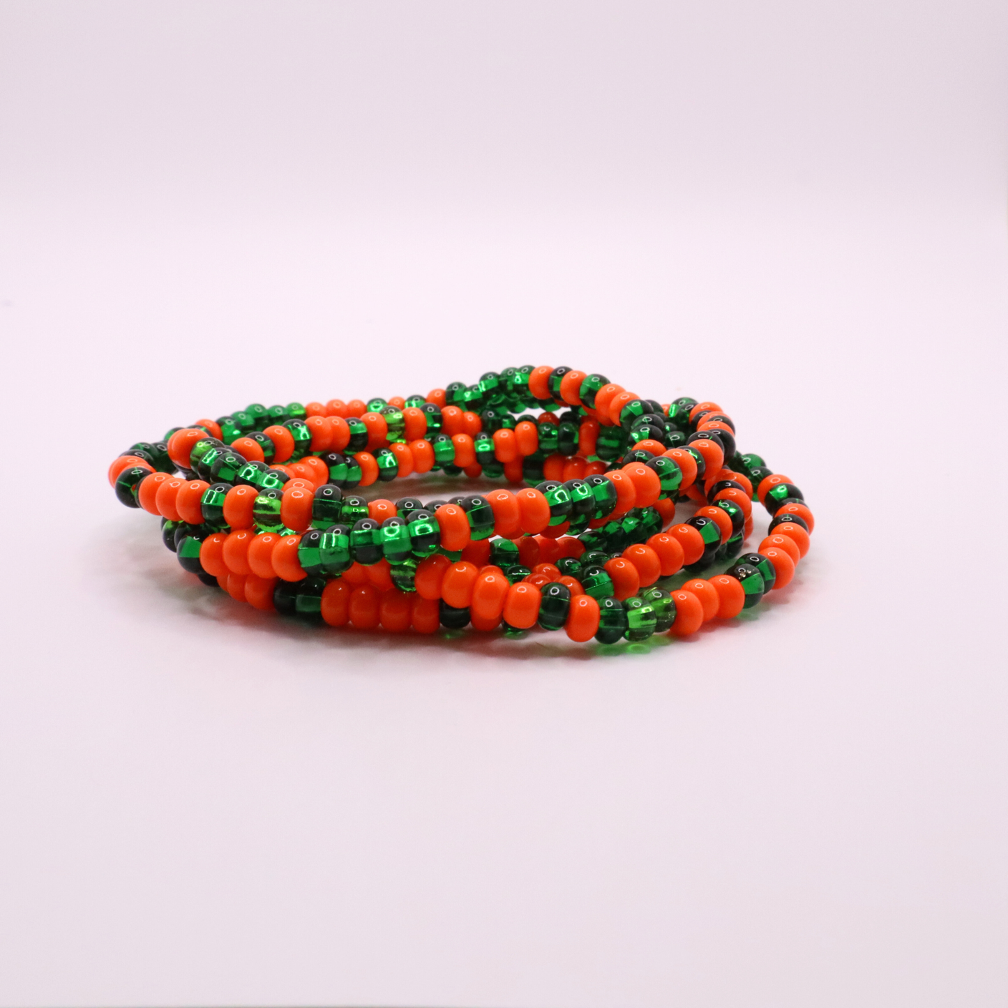 Set of six orange and green seed bead stretch bracelets featuring random orange and green seed beads on a white background
