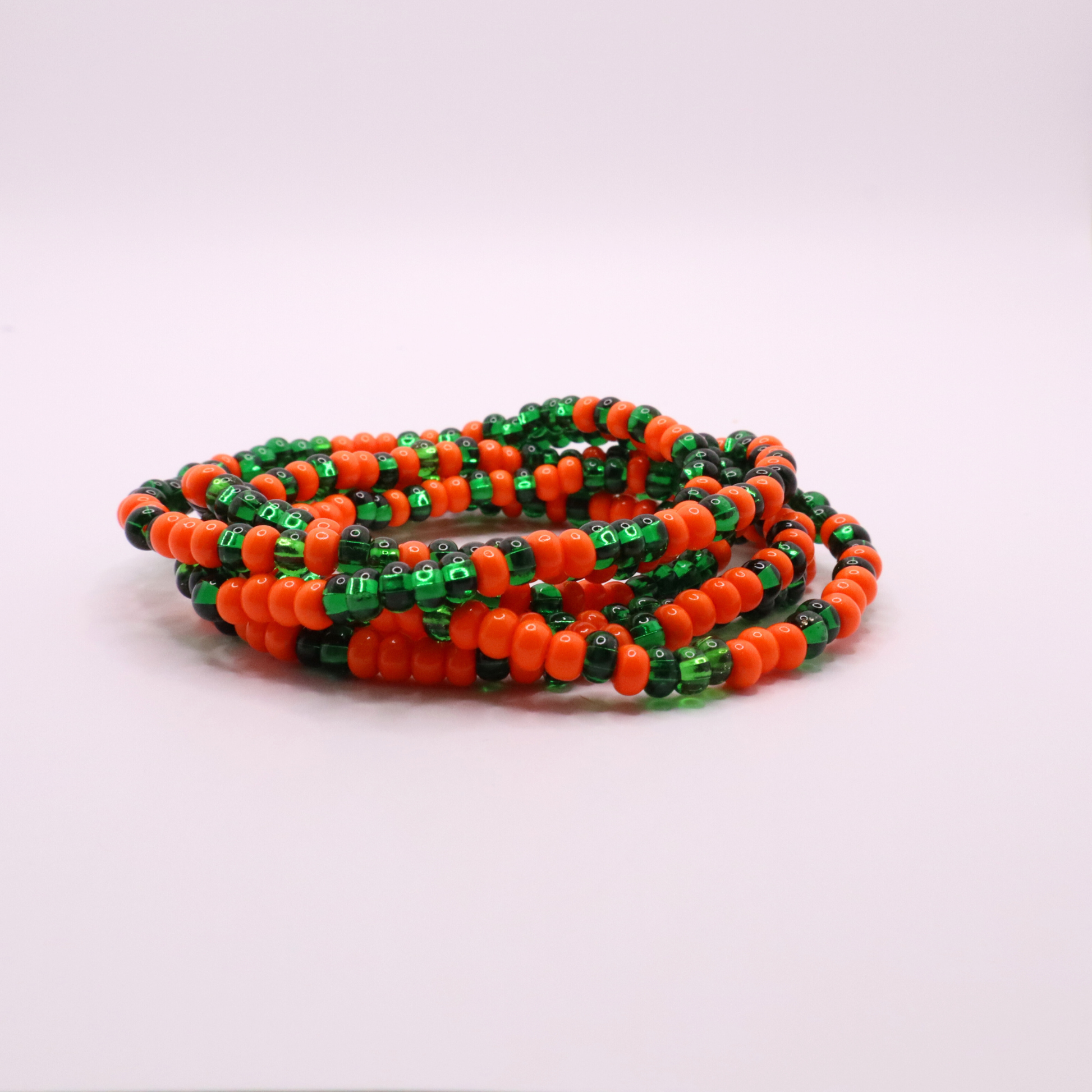 Set of six orange and green seed bead stretch bracelets featuring random orange and green seed beads on a white background