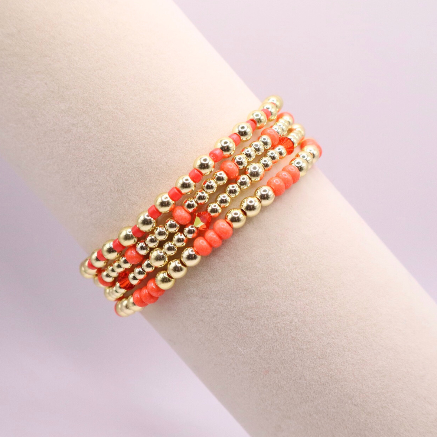 Stack of handmade stretch bracelets featuring vibrant coral Preciosa seed beads, faceted crystal accents, and polished gold-tone hematite beads on a clean white background.