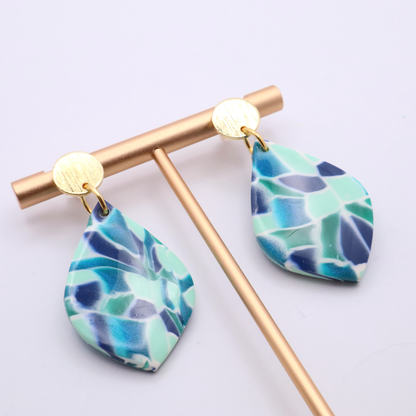 Teardrop earrings in blue, teal, and mint tones with 18k gold plated studs displayed on gold earring stand