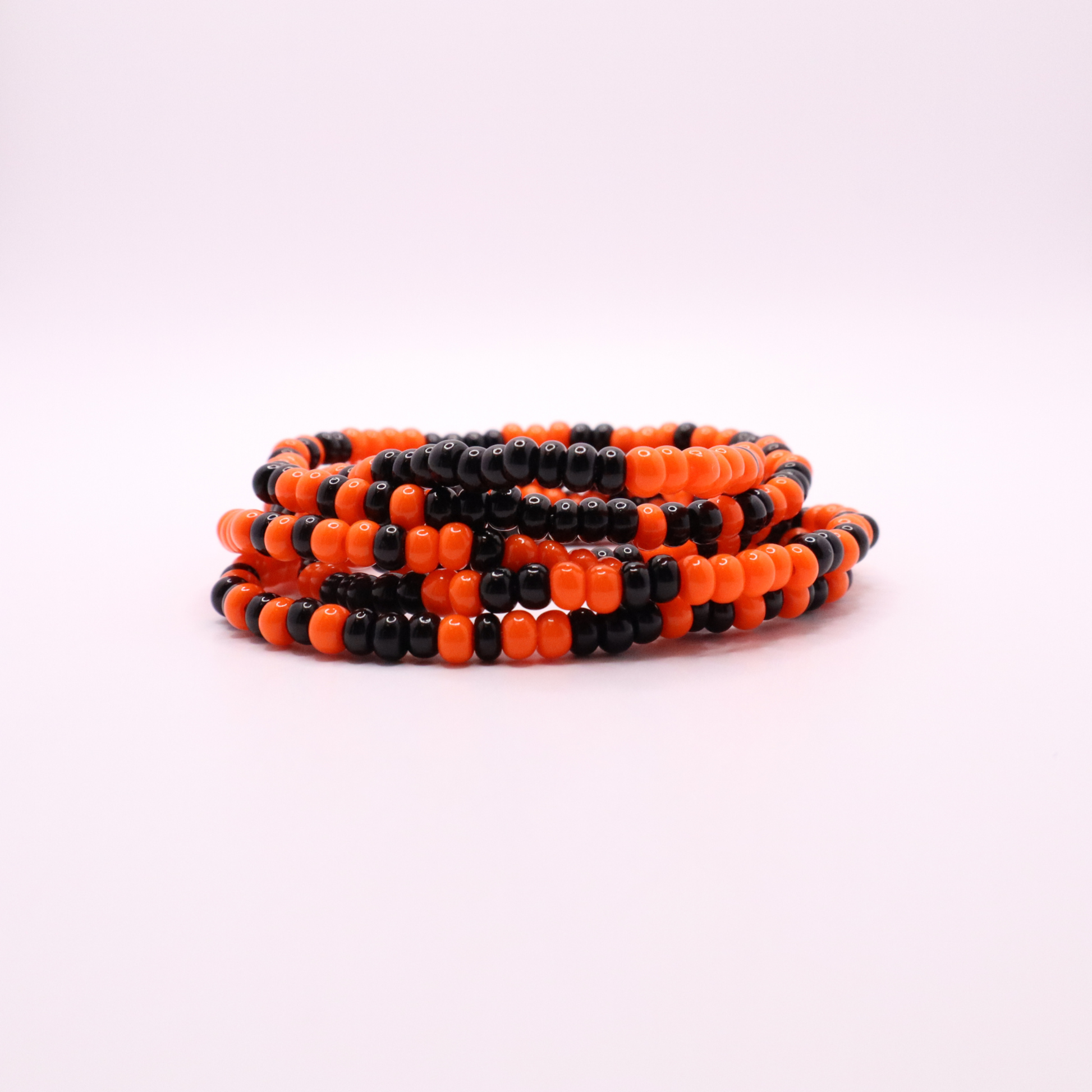 Set of six orange and black seed bead stretch bracelets featuring random orange and black seed beads on a white background