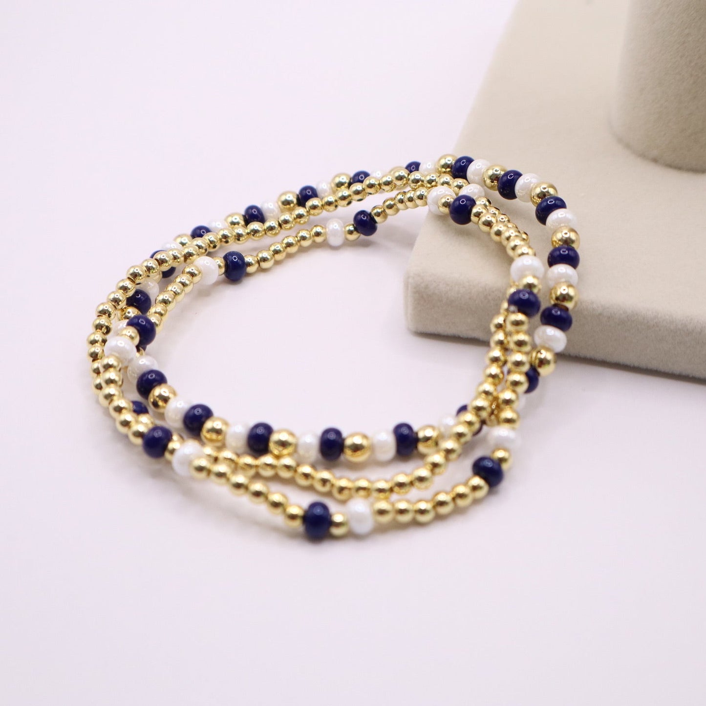 Multistrand beaded bracelet with gold, blue, and white beads on a white surface.