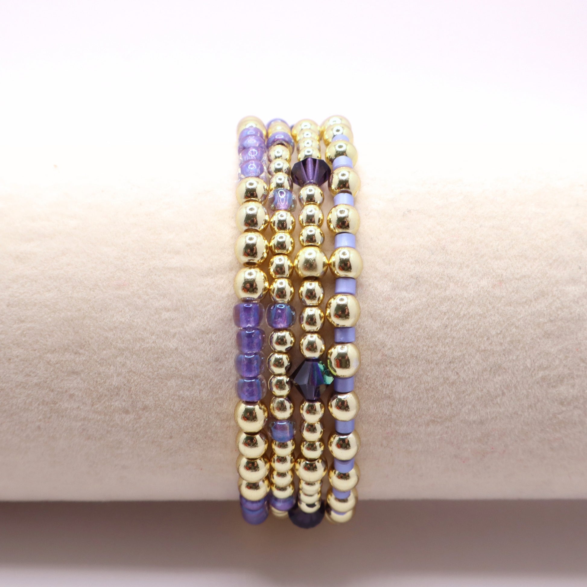 Handmade stretch bracelets in lavender and gold tones styled together as a layered jewelry stack.