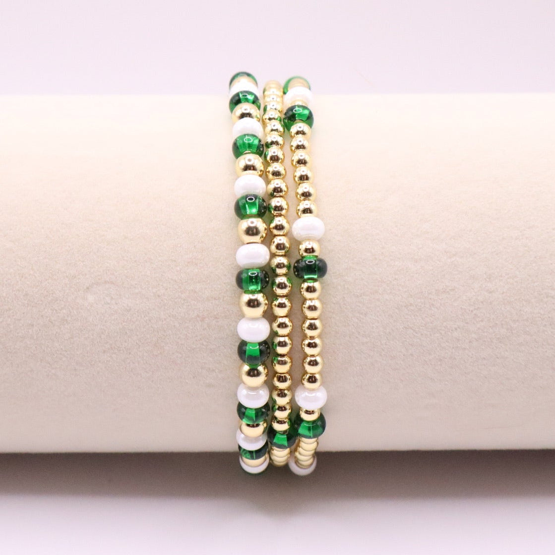 Three green, white, and gold beaded bracelets on a beige surface.
