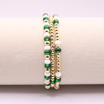 Three green, white, and gold beaded bracelets on a beige surface.