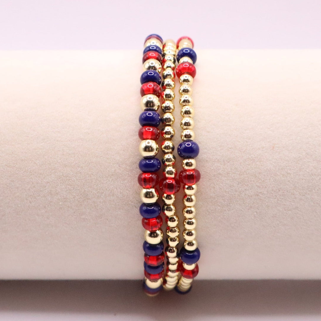 Three beaded bracelets in red, blue, and gold on a white surface