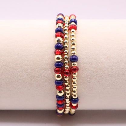 Three beaded bracelets in red, blue, and gold on a white surface