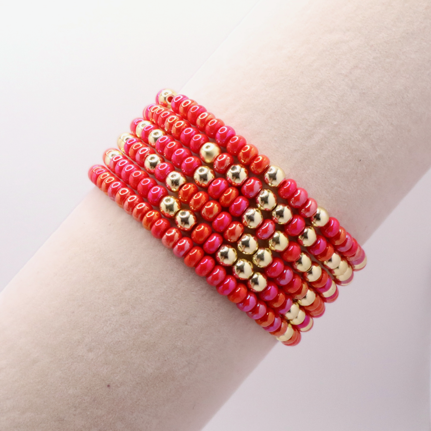 Stack of pink and gold beaded bracelets on a wrist against a light background