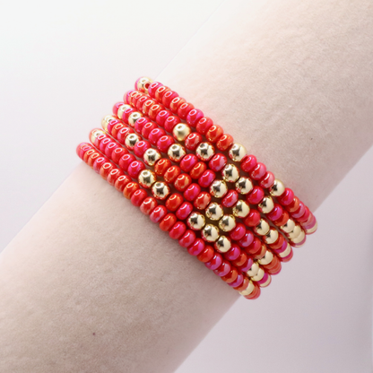 Stack of pink and gold beaded bracelets on a wrist against a light background