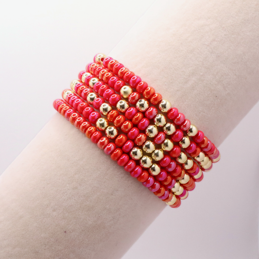Stack of pink and gold beaded bracelets on a wrist against a light background